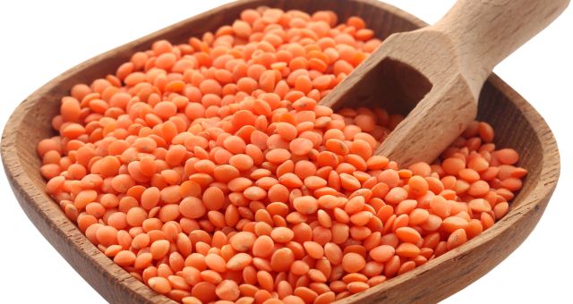 Image of a wooden bowl filled with red lentils and a wooden scoop in bowl.