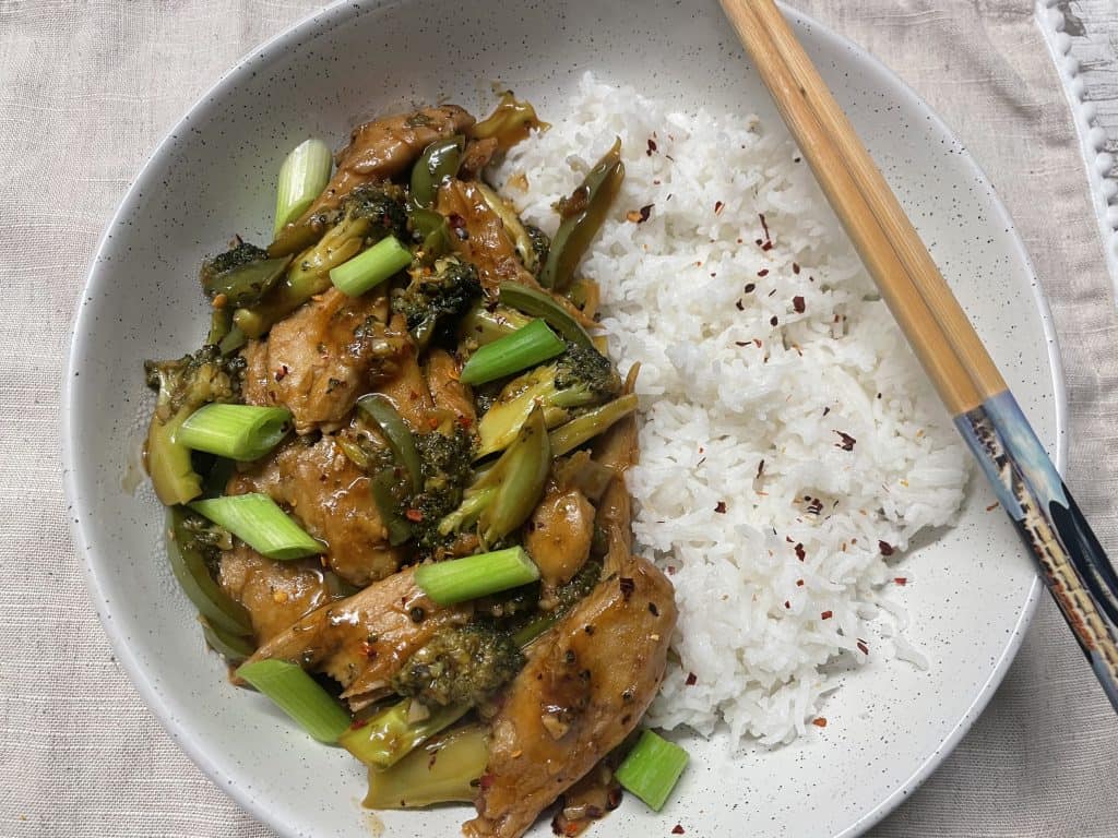 Mongolian beef and broccoli served in white bowl with chopsticks to side.