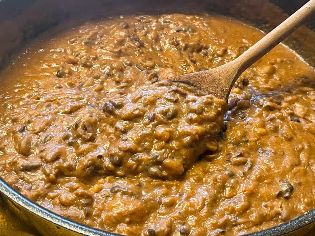 Refried beans cooked in a pan with a wooden spoon stirring.