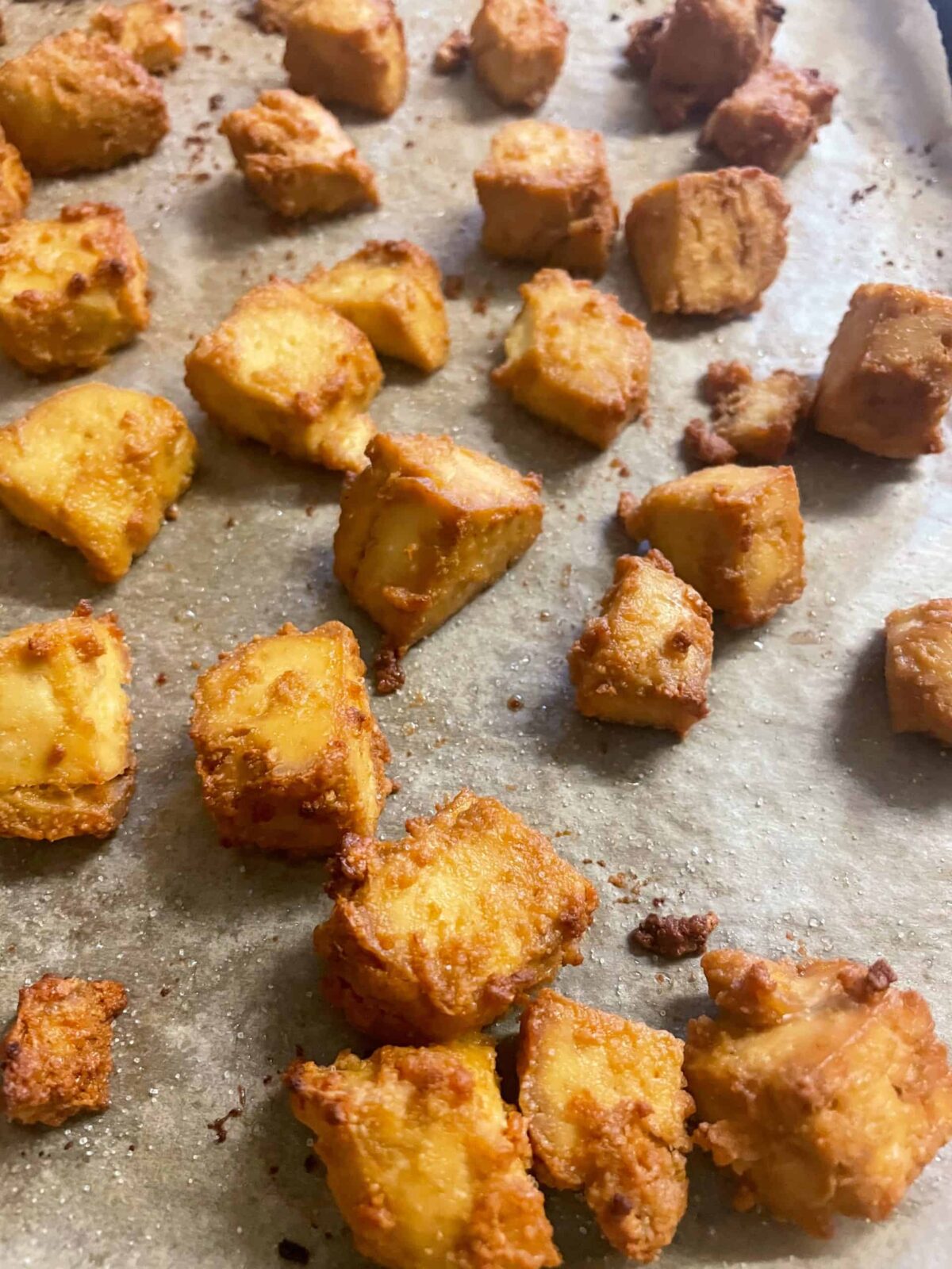 vegan crispy tofu bites sitting on greaseproof paper on baking tray.