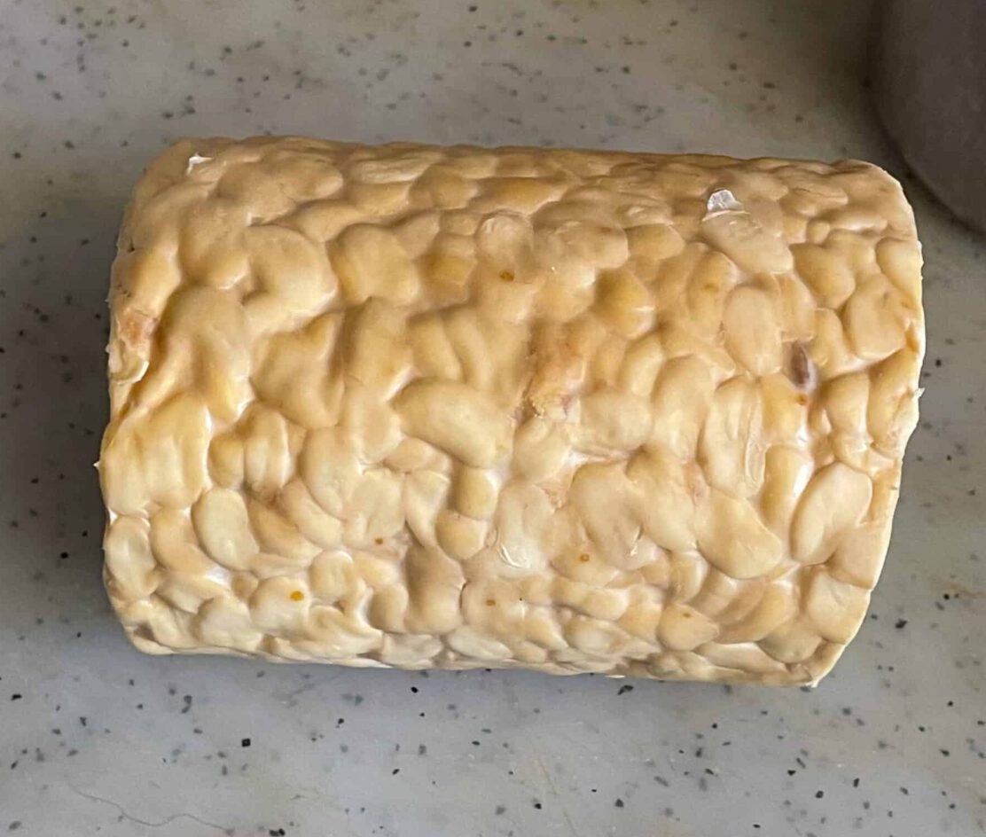 a slab of tempeh on a white chopping board.