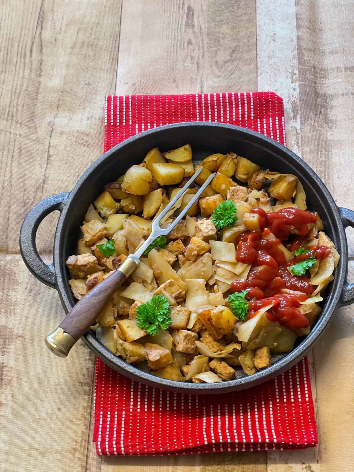 vegan corned beef hash in a cast iron skillet pan with red tea towel underneath and wooden background.