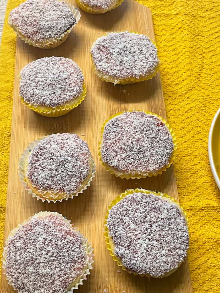 traditional vegan vanilla fairy cakes decorated with jam and coconut and on a yellow tea towel.