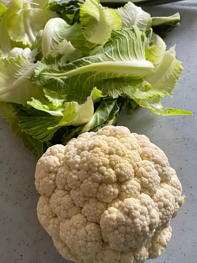 whole cauliflower with leaves removed and to the side on a white chopping board.