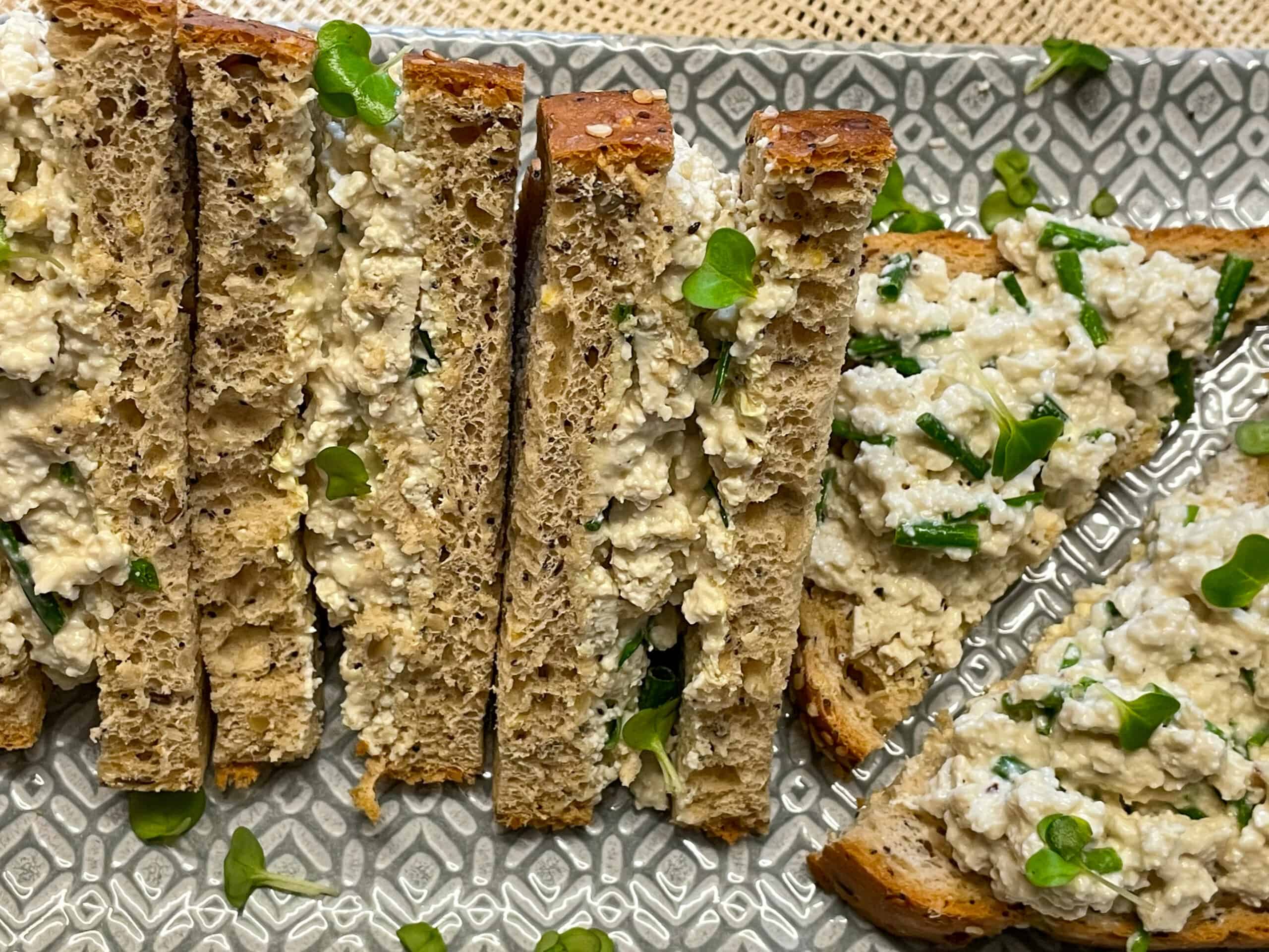 A row of tofu sandwiches on a stripy grey platter.