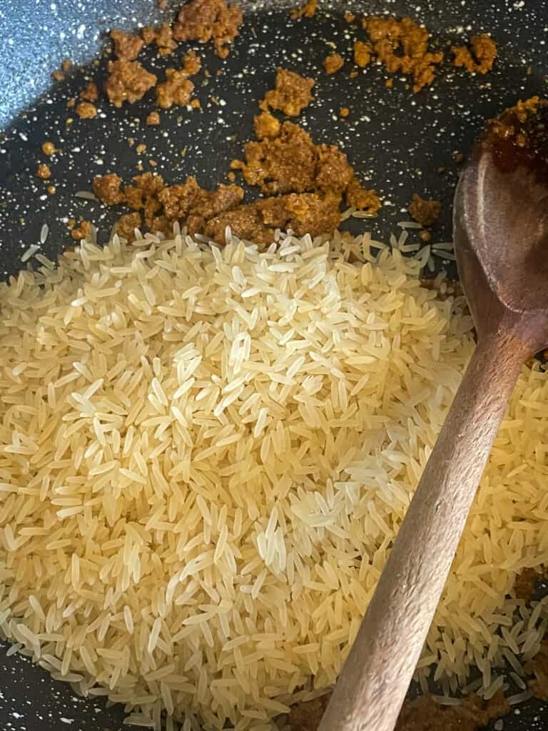 Long grain rice with curry powder in a granite skillet pan with wooden spoon.