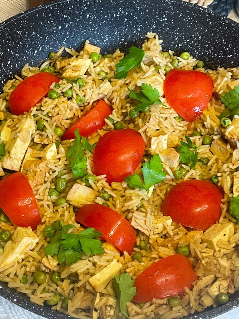 vegan kedgeree with red tomatoes and parsley in a shallow pan ready to serve.