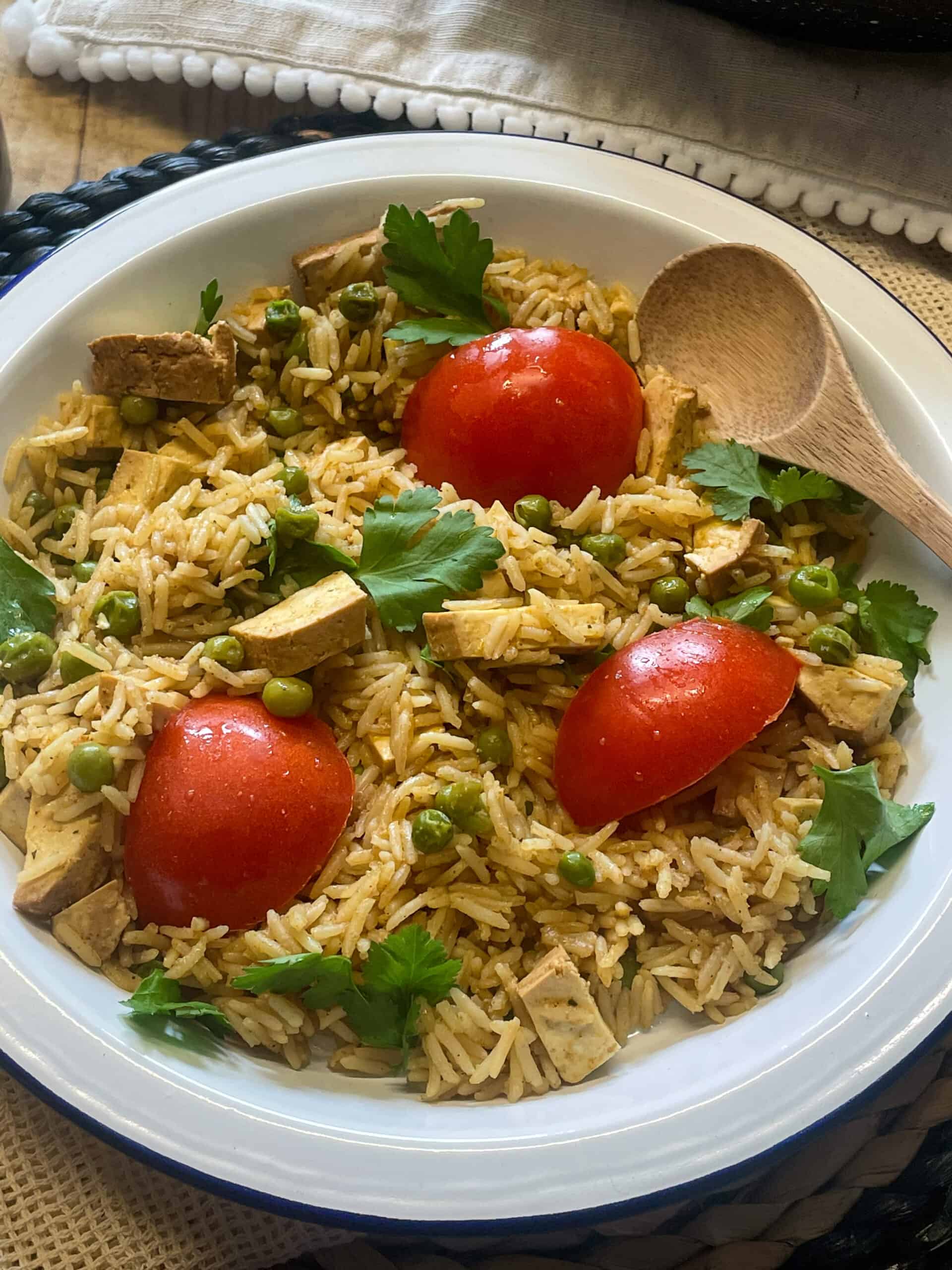 vegan smoked tofu kedgeree rice and tomatoes with coriander, in a bowl with small wooden spoon.