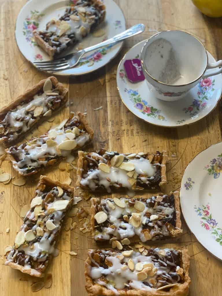 Vegan Scottish Border Tart featured image, slices of Border tart on wooden chopping board with tea cup and saucer, and serving plate with pink flowery old fashioned pattern.