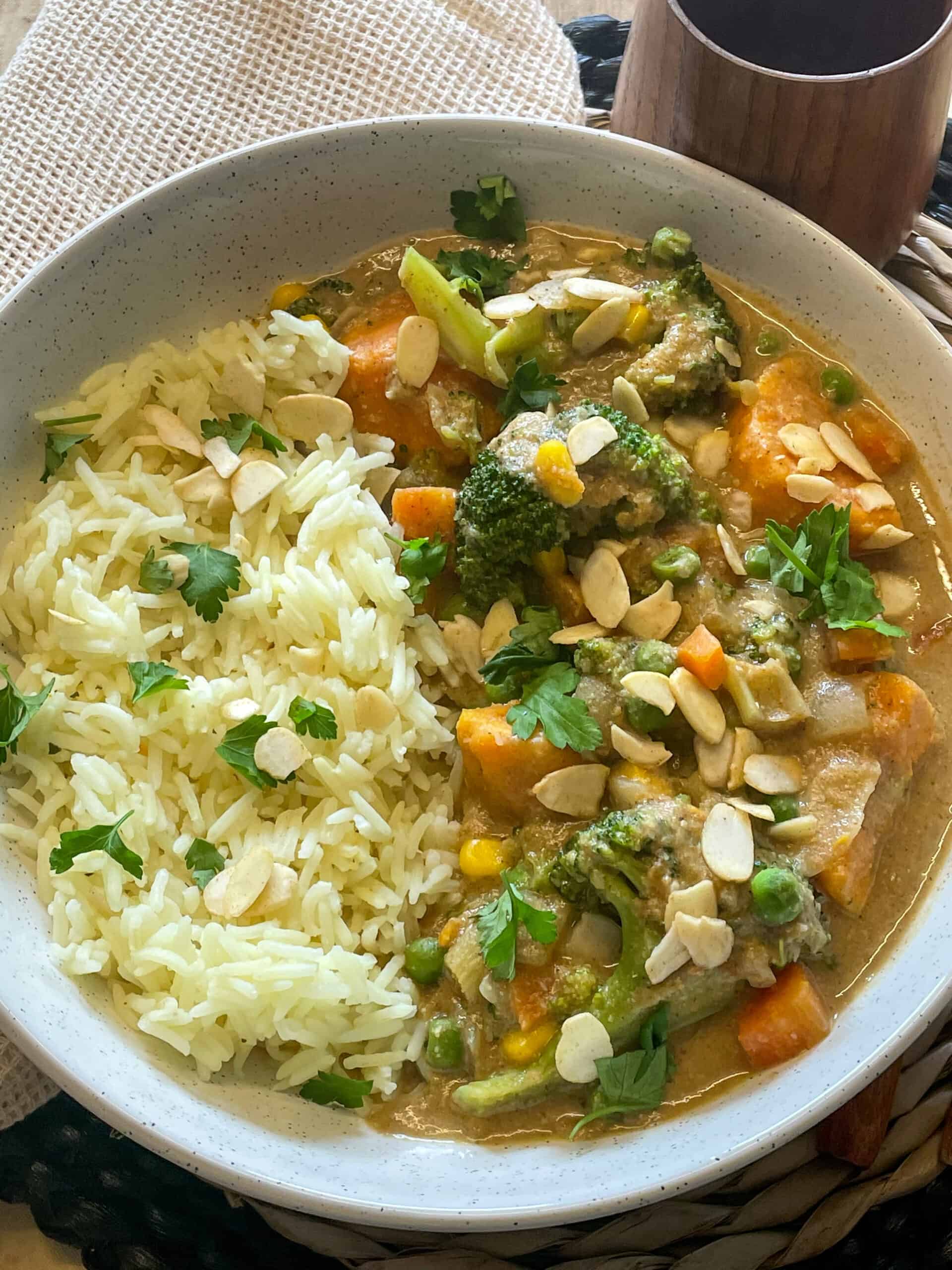 A close up of a bowl of the best vegetable curry with a small brown cup to the side.