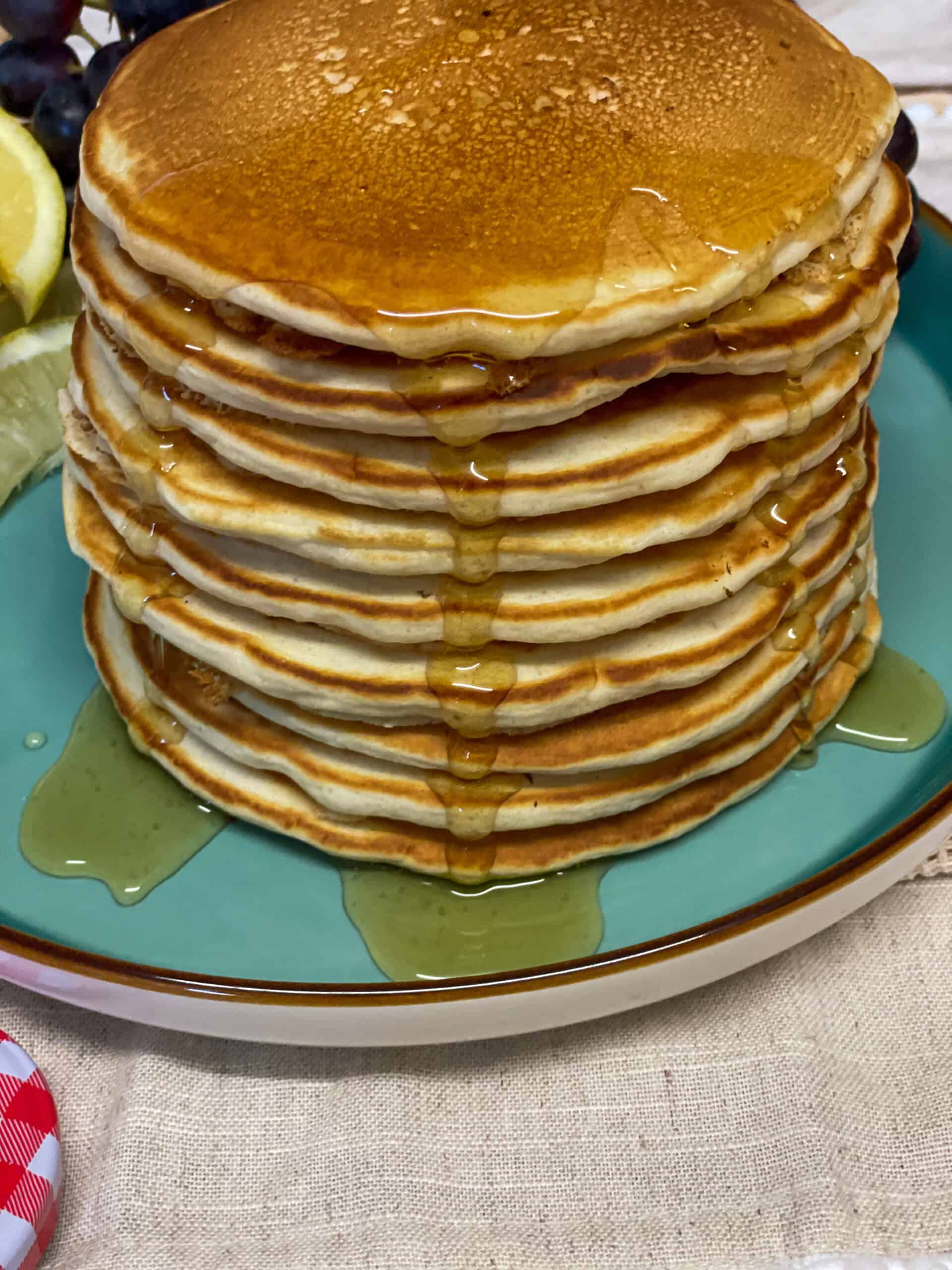 A stack of pancakes with syrup drizzling down the sides and on a turquoise plate.