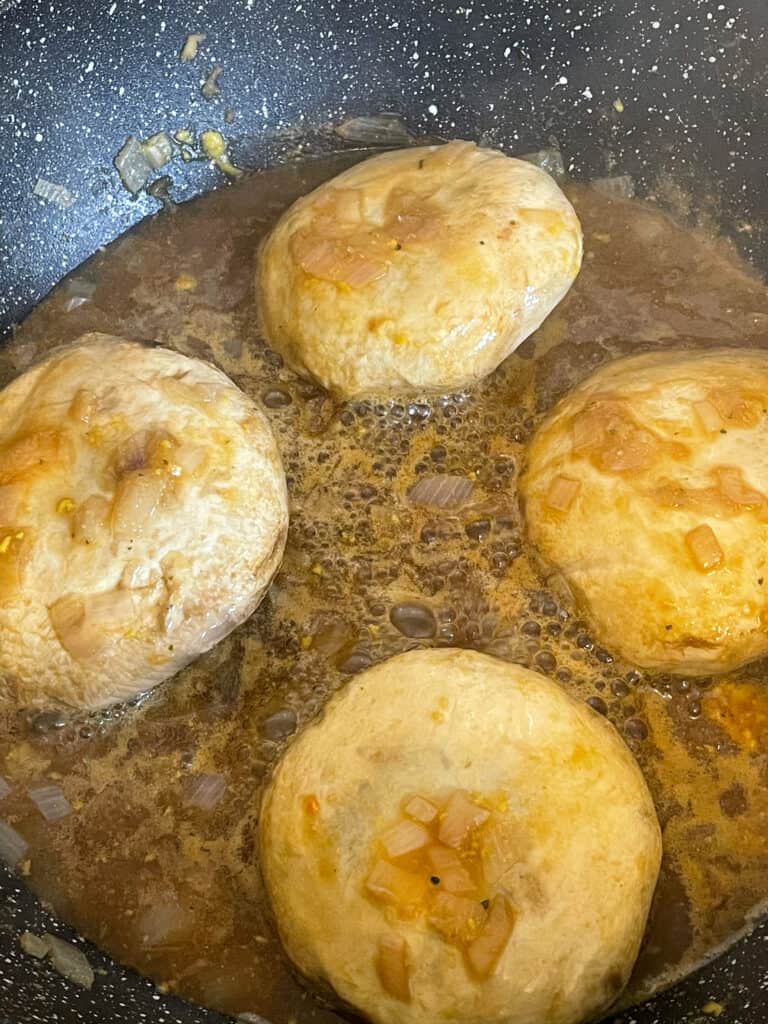 Four mushrooms cooking in pan.