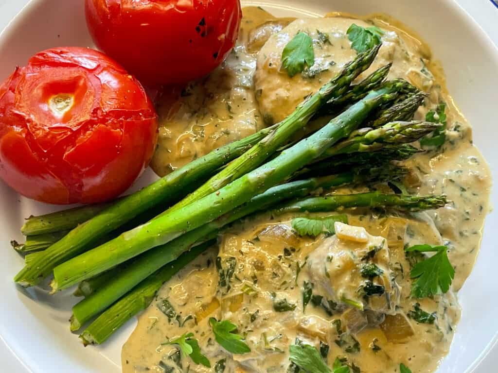 Vegan mushroom steak Diane served on white plate with side of asparagus and roast tomatoes.