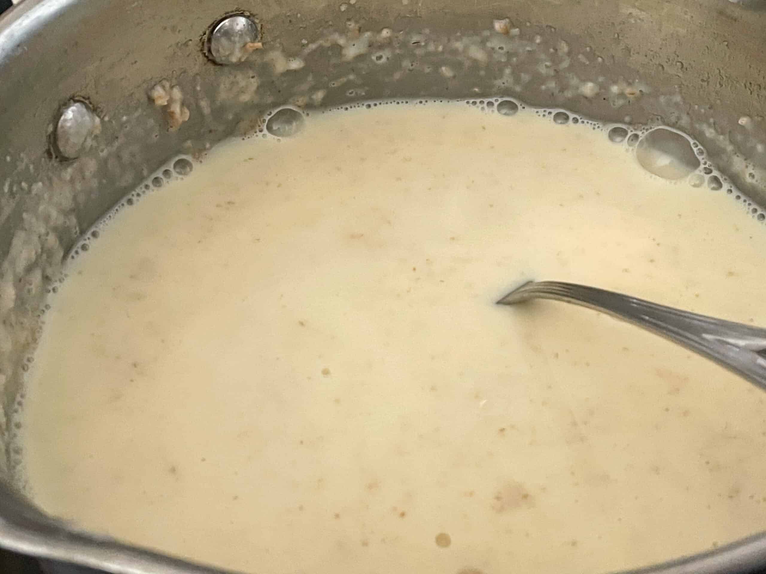 Milk added to roux and cooking on saucepan.