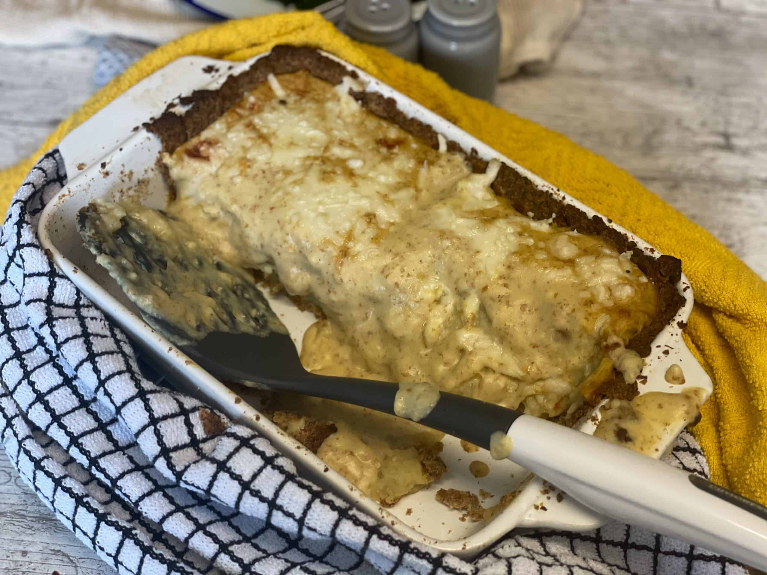 Cheese onion and potato pie in baking dish with spatula and tea cloth to side.