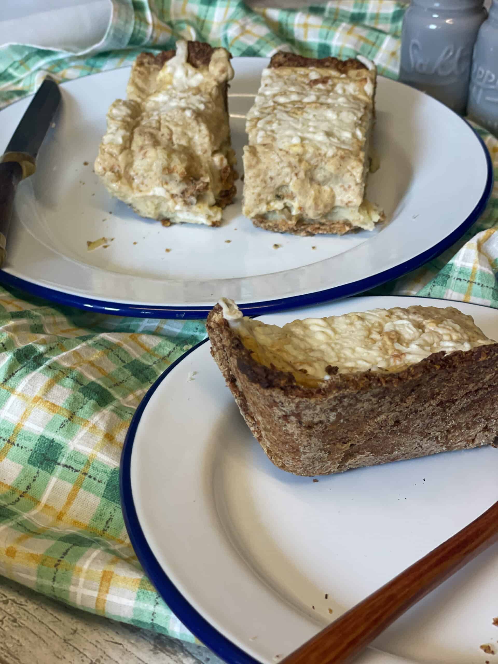 Two plates with a slice of cheese pie on each, green and yellow stripe table cloth picnic setting.