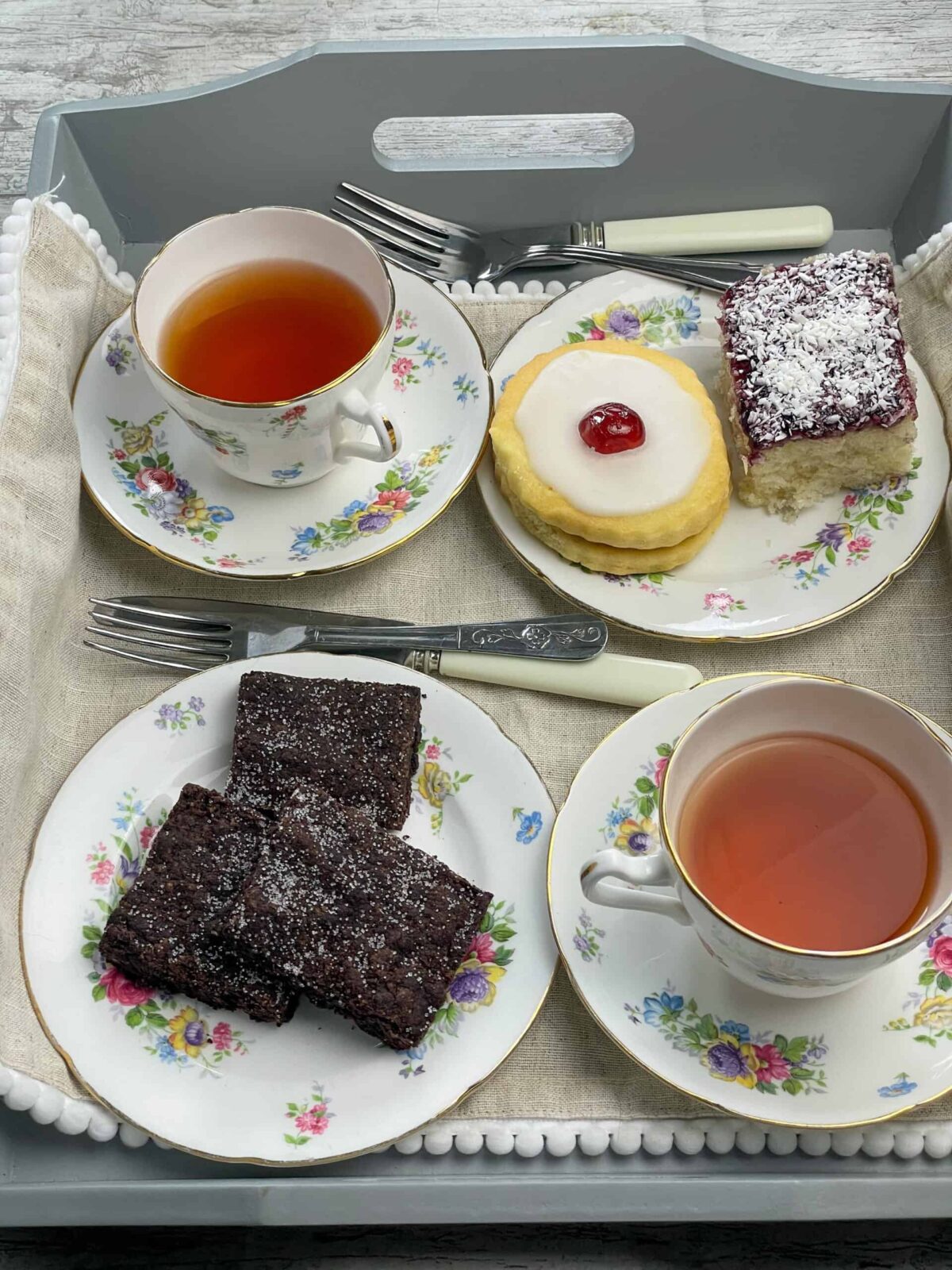 Afternoon tea tray with cookies and slices of concrete cake, flower patterned tea cup and saucers. 