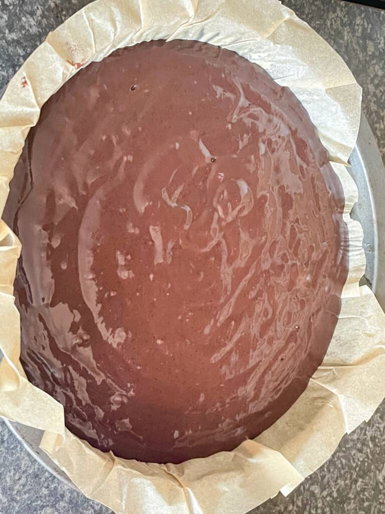 Unbaked chocolate cake in a baking pan lined with greaseproof paper.