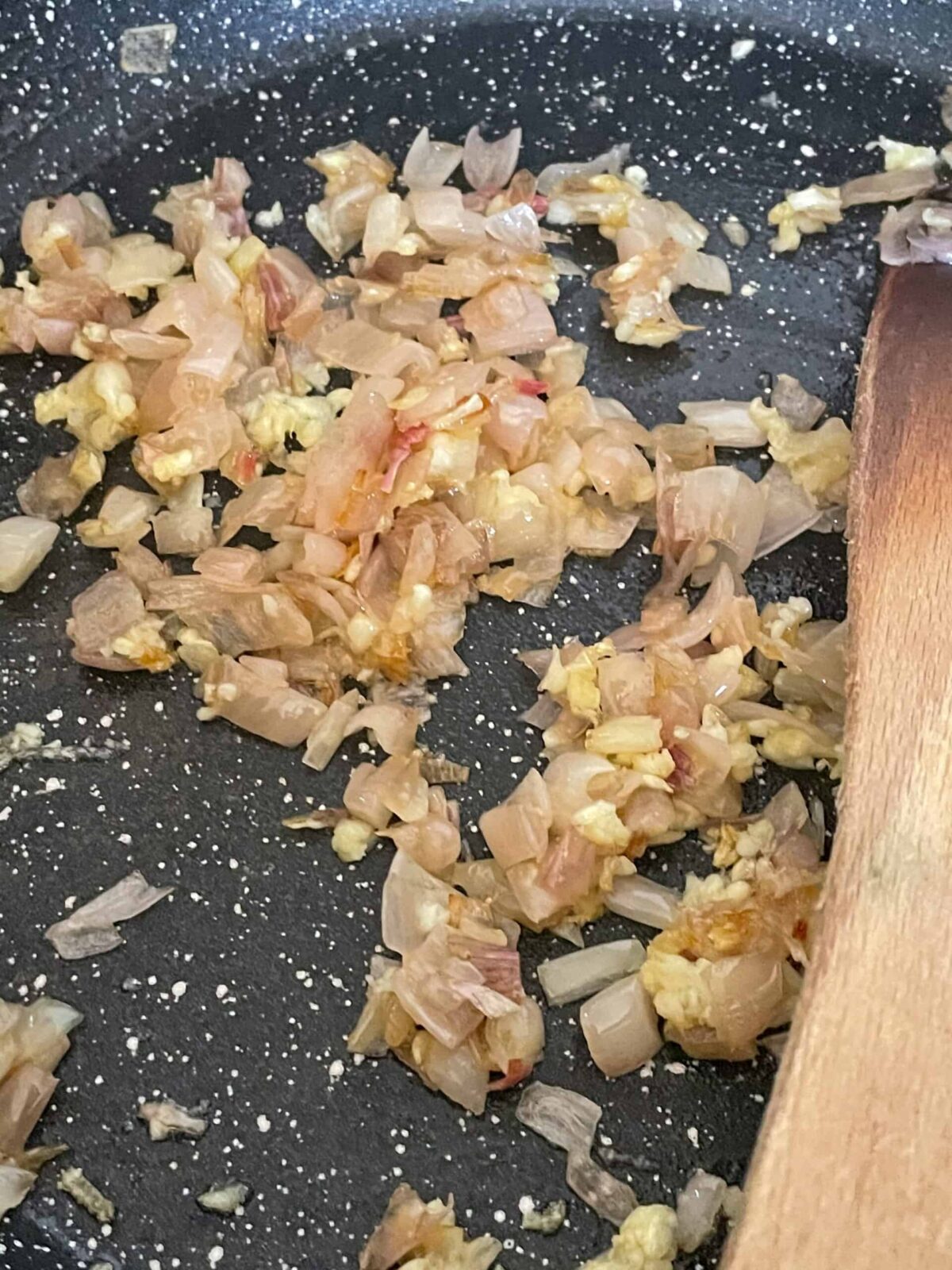 shallots cooking in the skillet with a wooden spatula.