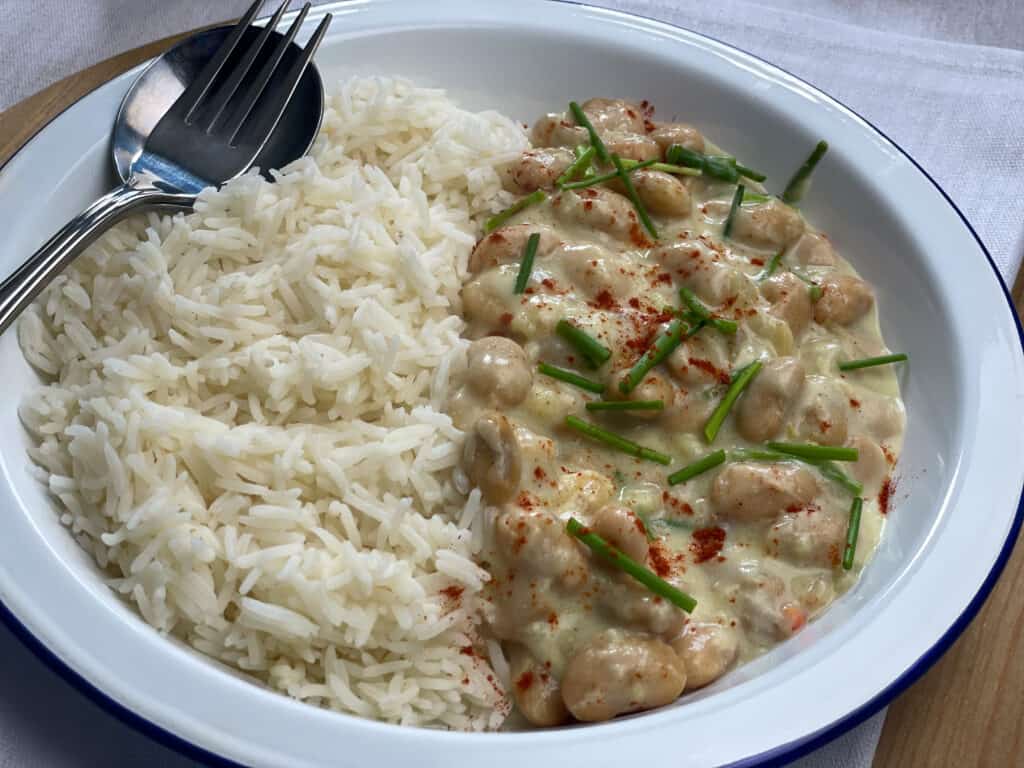 Vegan butterbean chicken supreme with white boiled rice served on a white bowl with a spoon and fork displayed at the side