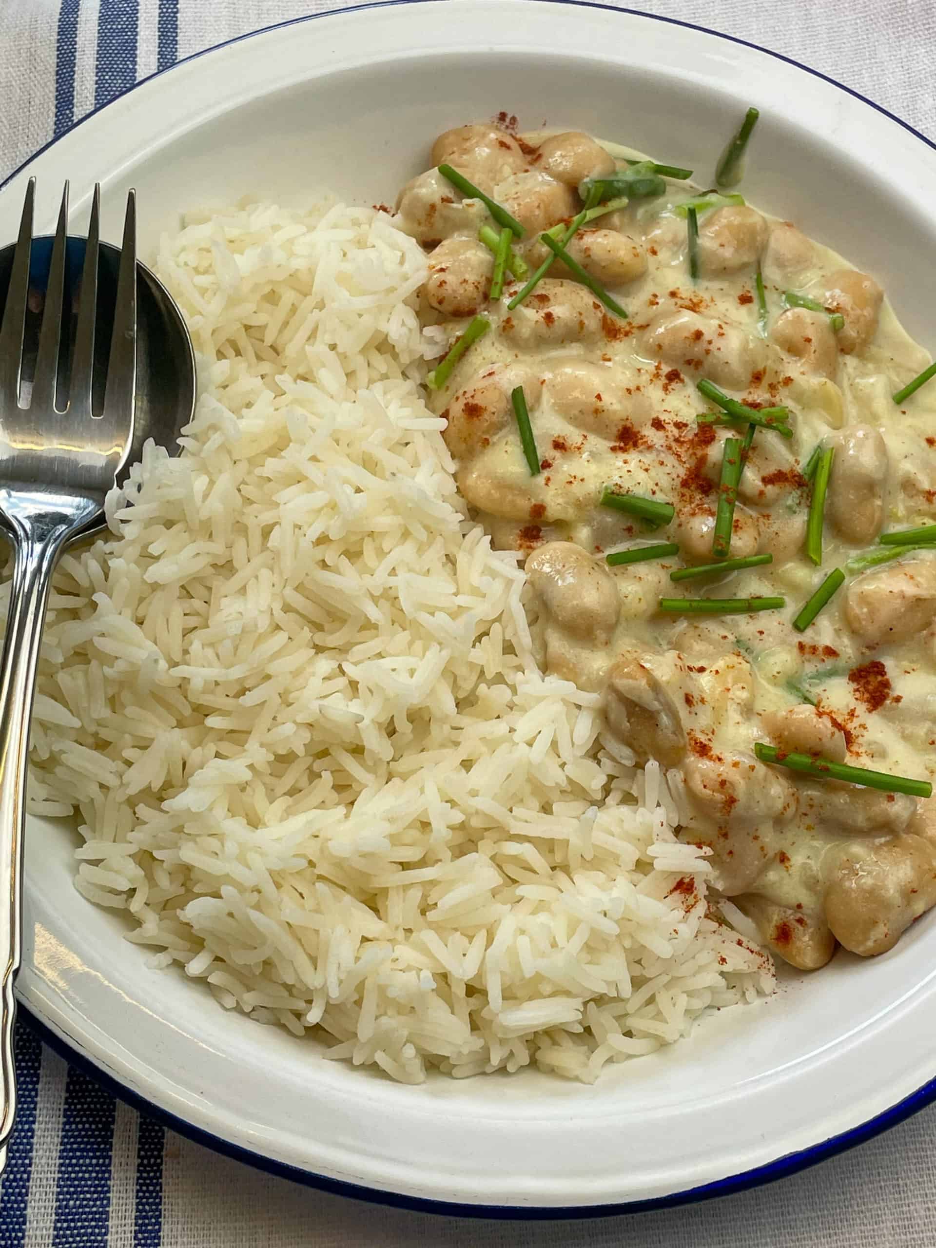 Butter bean 'chicken' supreme served with rice, spoon and fork at the side and blue striped tea towel, featured image.