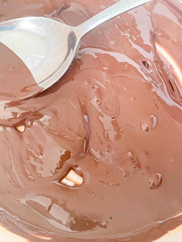chocolate melted and ready to mix through the frosting in a small bowl with silver spoon.