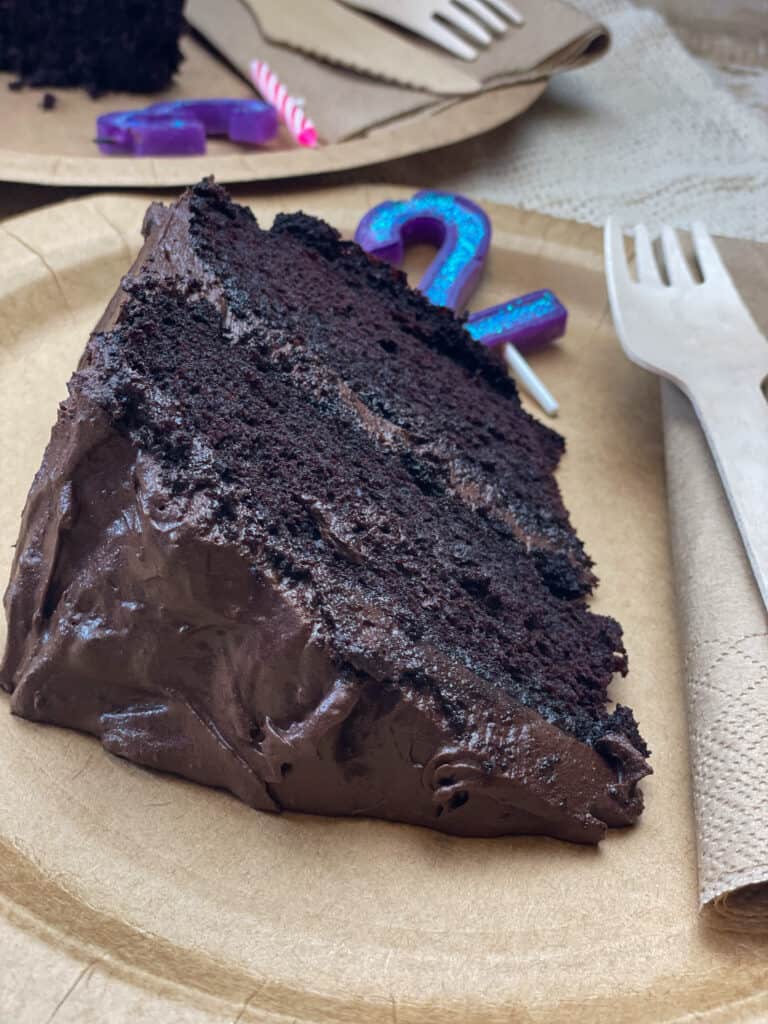 slice of vegan gluten-free chocolate cake on brown disposable plate with birthday candles, fork and napkin