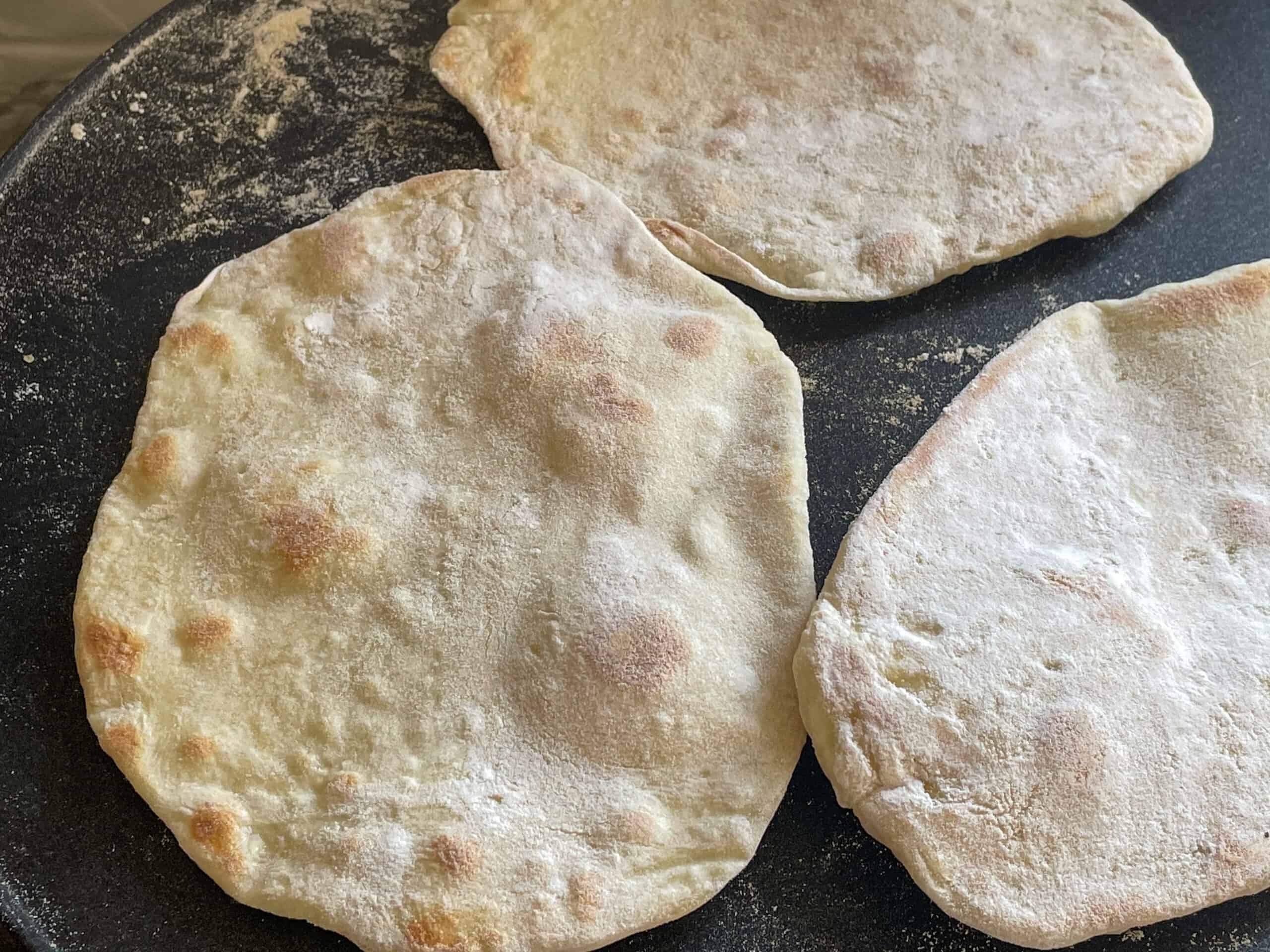 Flatbreads cooking on a hotplate with large bubbles forming on the cooking flatbreads.