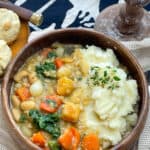 Medieval potage stew served in a wooden bowl, with fork and spoon, little bread rolls at the side, and candlestick