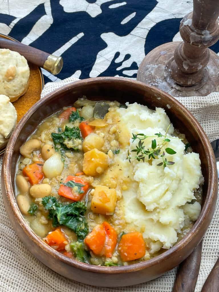 Medieval potage stew served in a wooden bowl, with fork and spoon, little bread rolls at the side, and candlestick