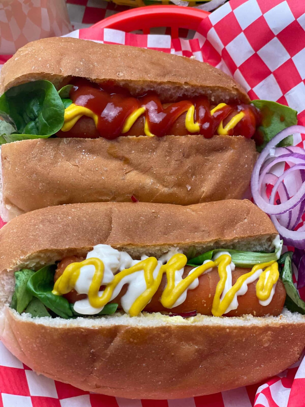 carrot hotdogs in a long bread bun with mustard, ketchup drizzles, and green salad, with a red check mat underneath.