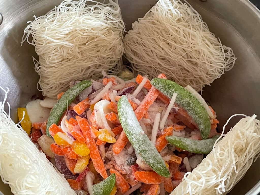 dried rice noodles and frozen veggies added to soup pan.