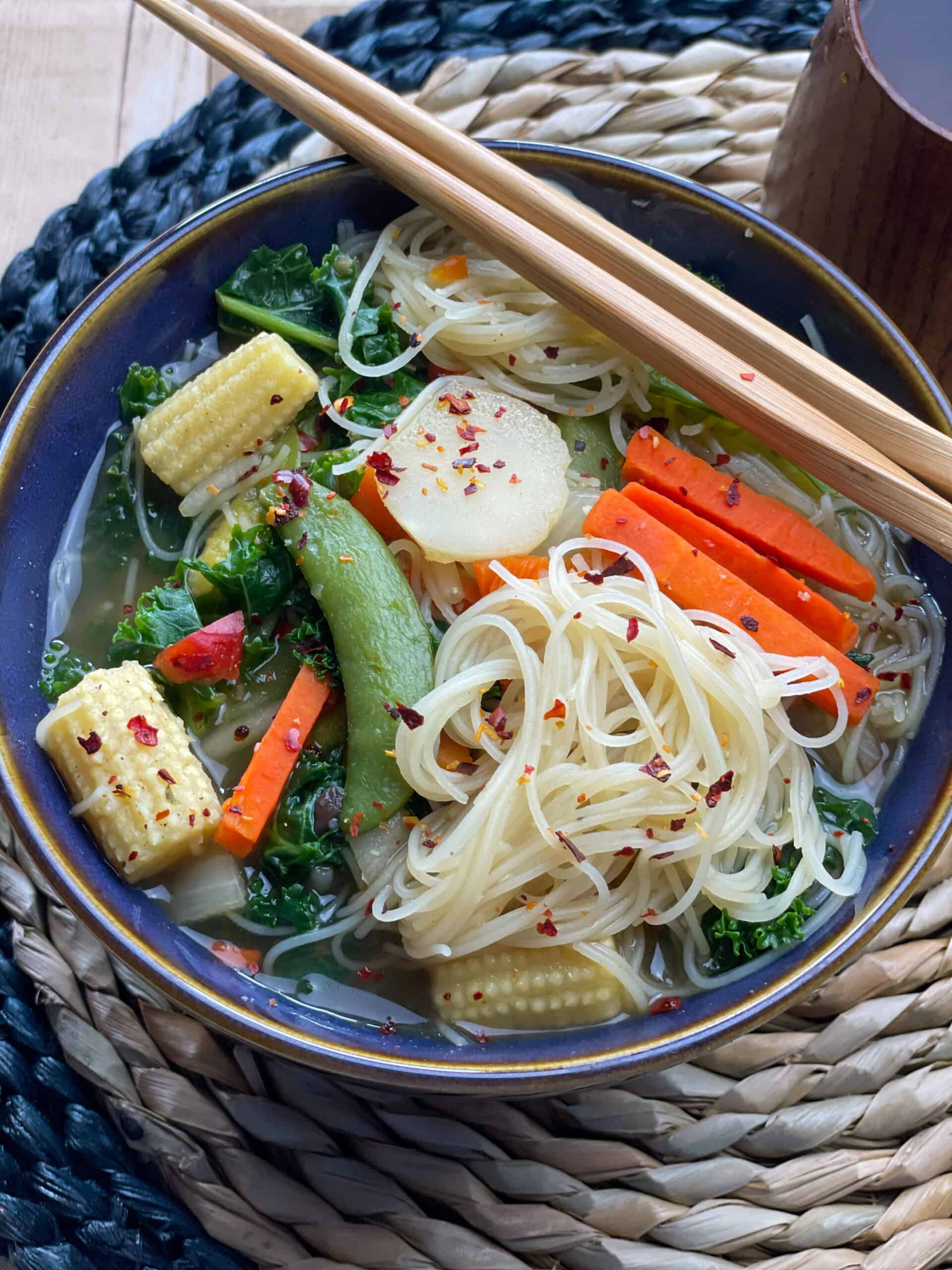 stir fry soup served in blue bowl with gold rim, chop sticks to the side, and sitting on a wicker mat, featured image.