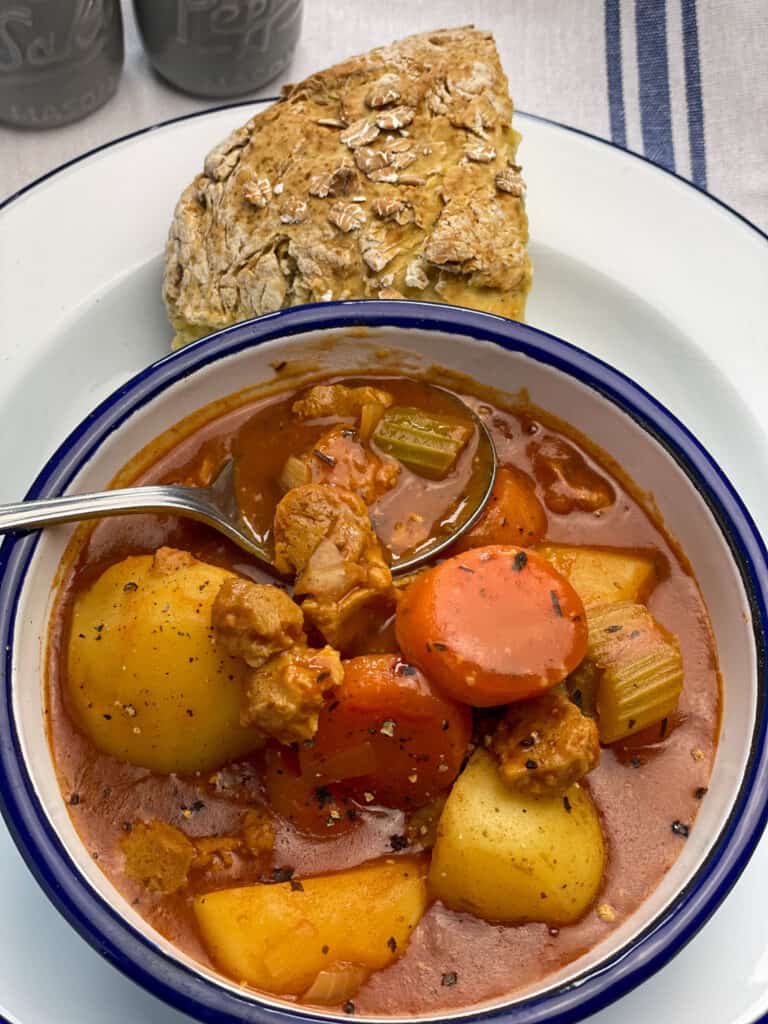 vegan beef stew served in white bowl with blue rim, crusty bread on side and salt and pepper dishes.