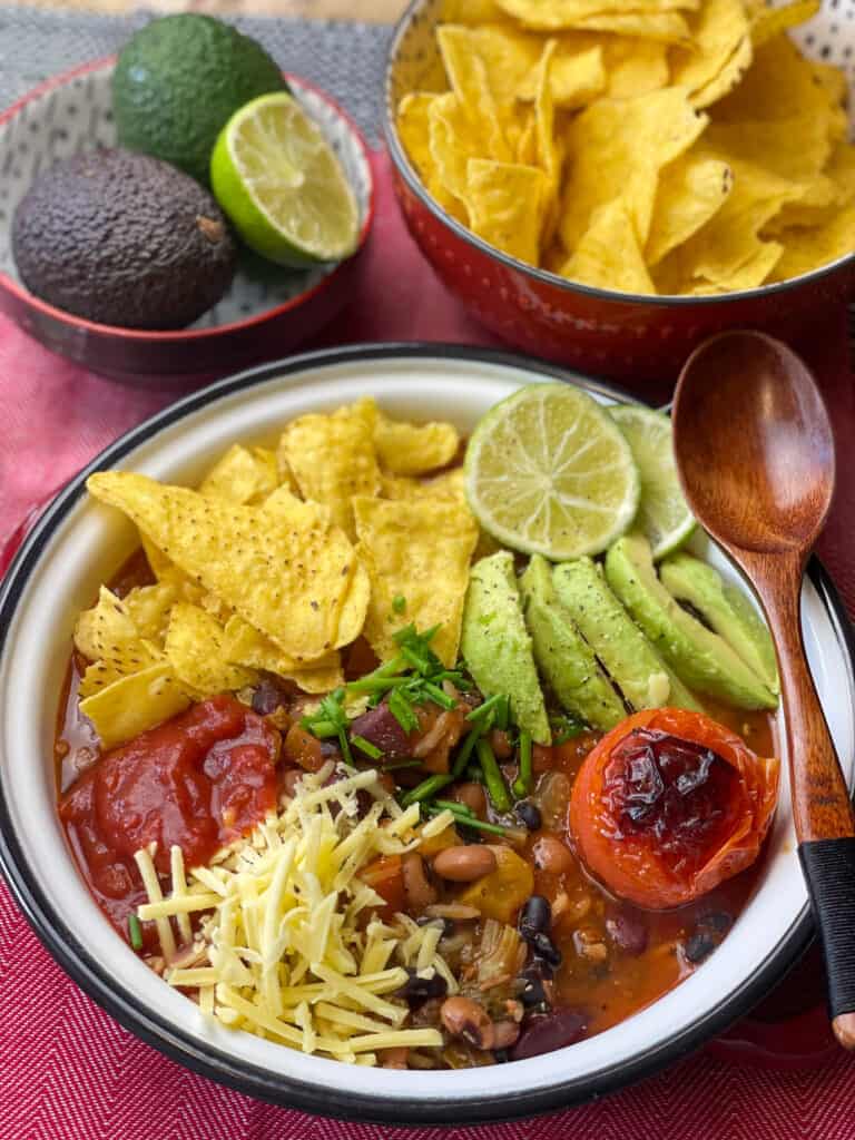 taco bean soup served in white enamel dish with toppings and garnishes. A red background.