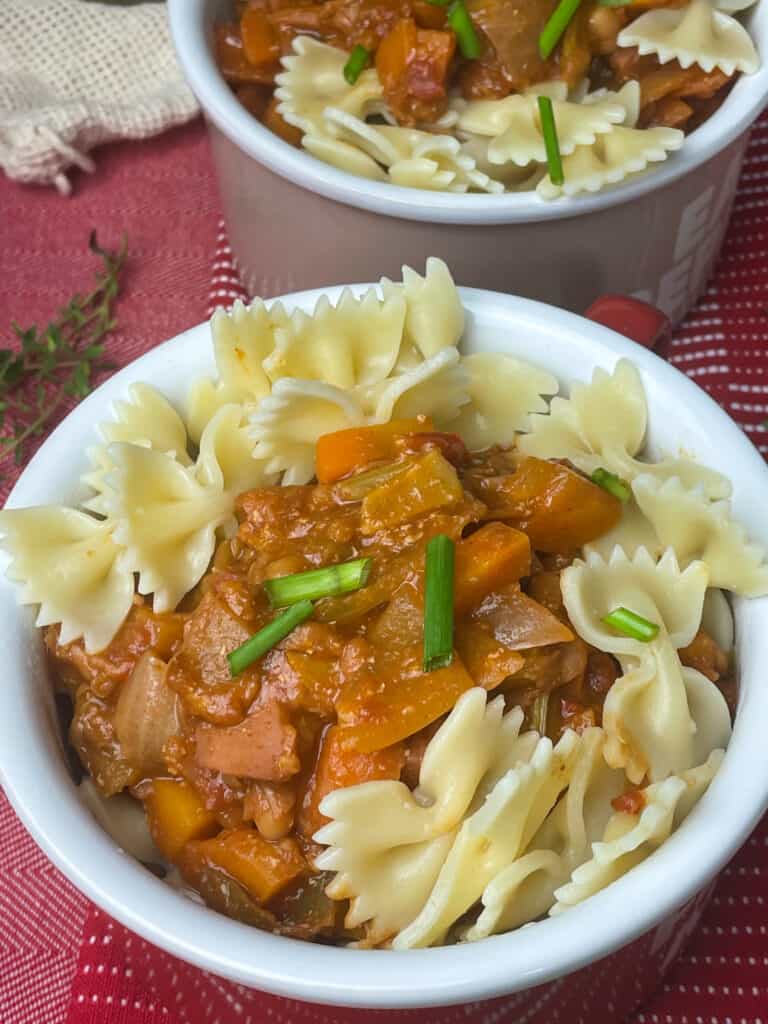 close up of camp fire stew in large mug served with pasta and chopped chives.