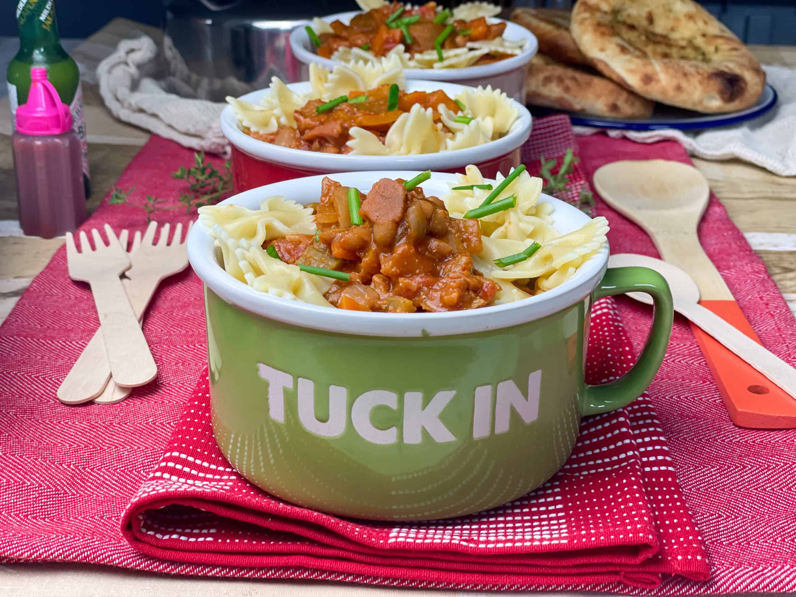 Large mug with the words 'tuck in' on a red mat and wooden forks to side, more mugs at back.