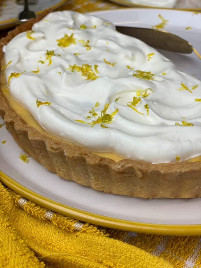 Pineapple tart with whipped cream topping and lemon zest, on white plate with yellow rim, yellow tea towel.