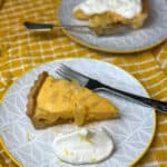 2 slices of pineapple tart, one with cream at side and the other with cream on top, dessert forks and yellow background.