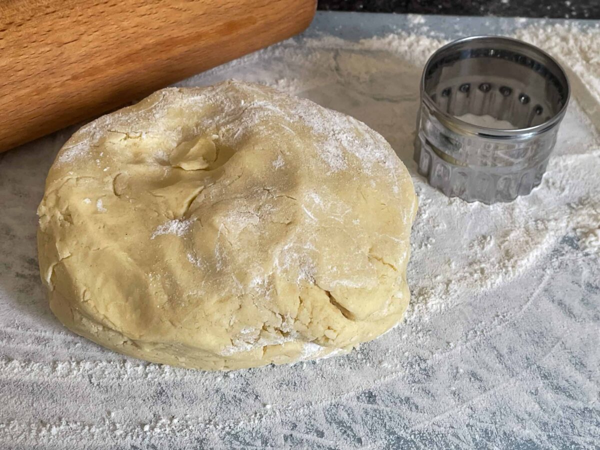 Biscuit dough brought together into a biscuit dough ball, biscuit cutter to side with a rolling pin, flour dusted on white board.