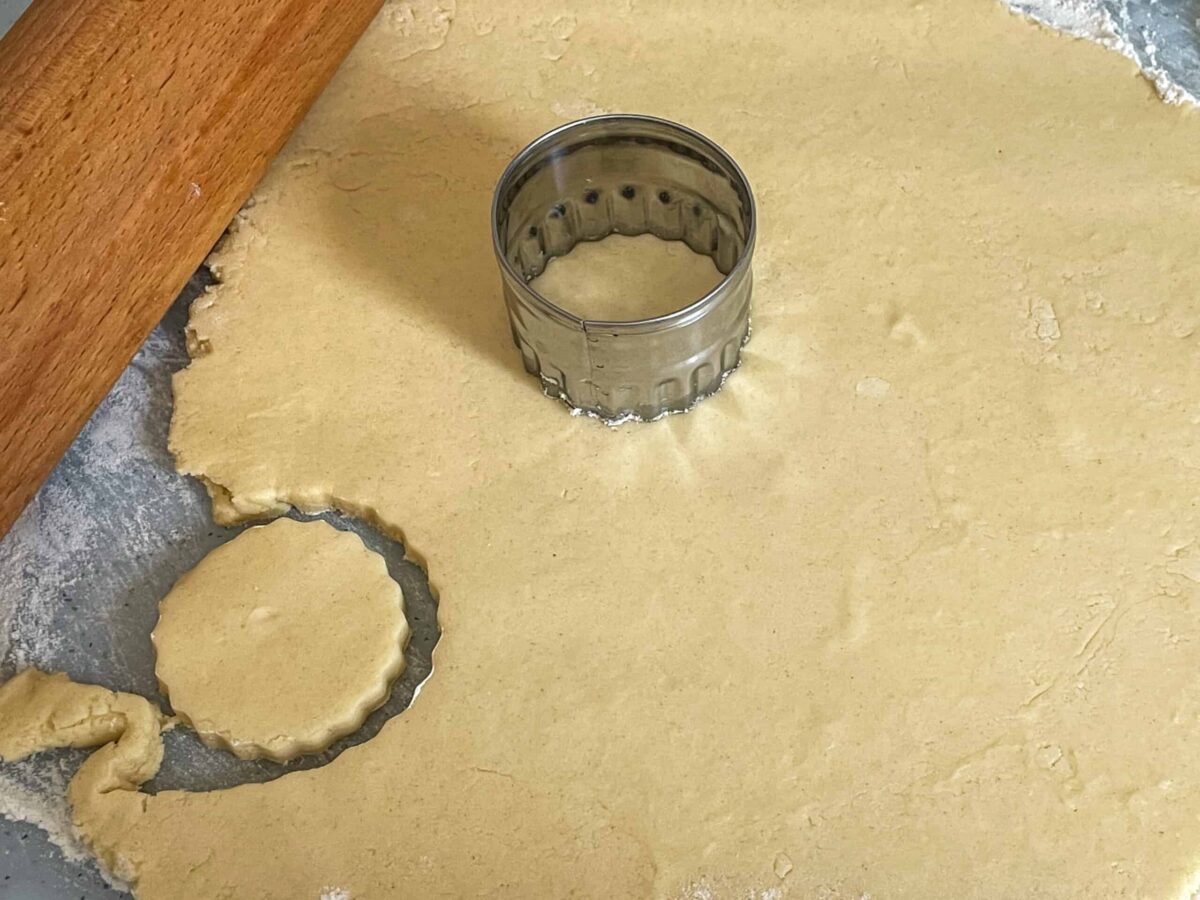 Biscuit dough rolled out and biscuit cutter on top, with stamped out biscuit shape, rolling pin to side.