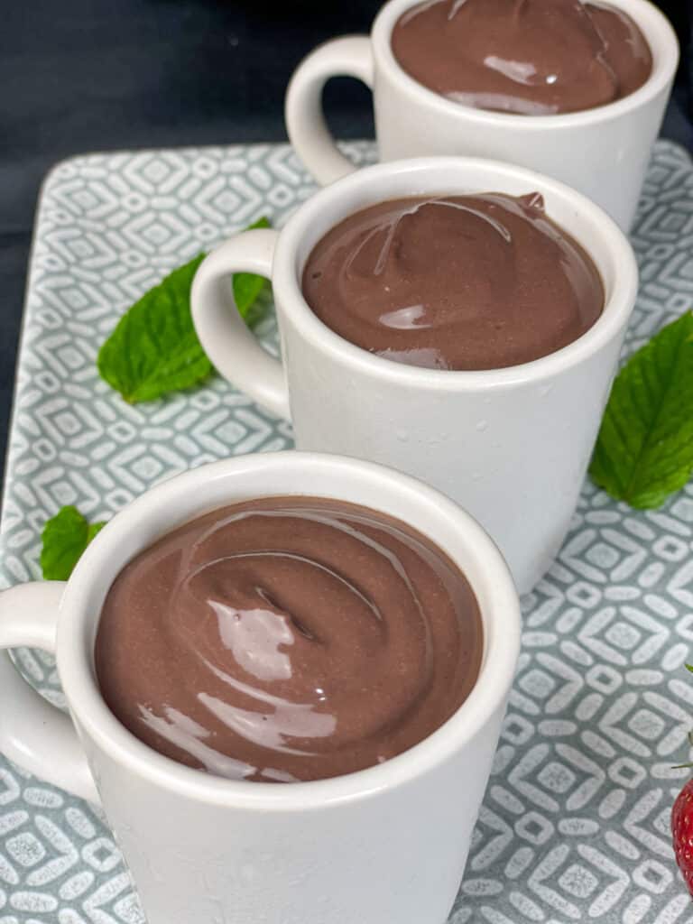 3 chocolate puddings in expresso mugs, grey plate, mint leaves and dark background, mint leaf garnish and grey and white tray..