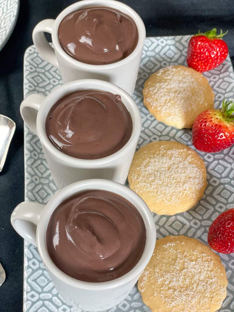 3 chocolate puddings in little expresso mugs with shortbread biscuits and strawberries, on a grey rectangular plate.