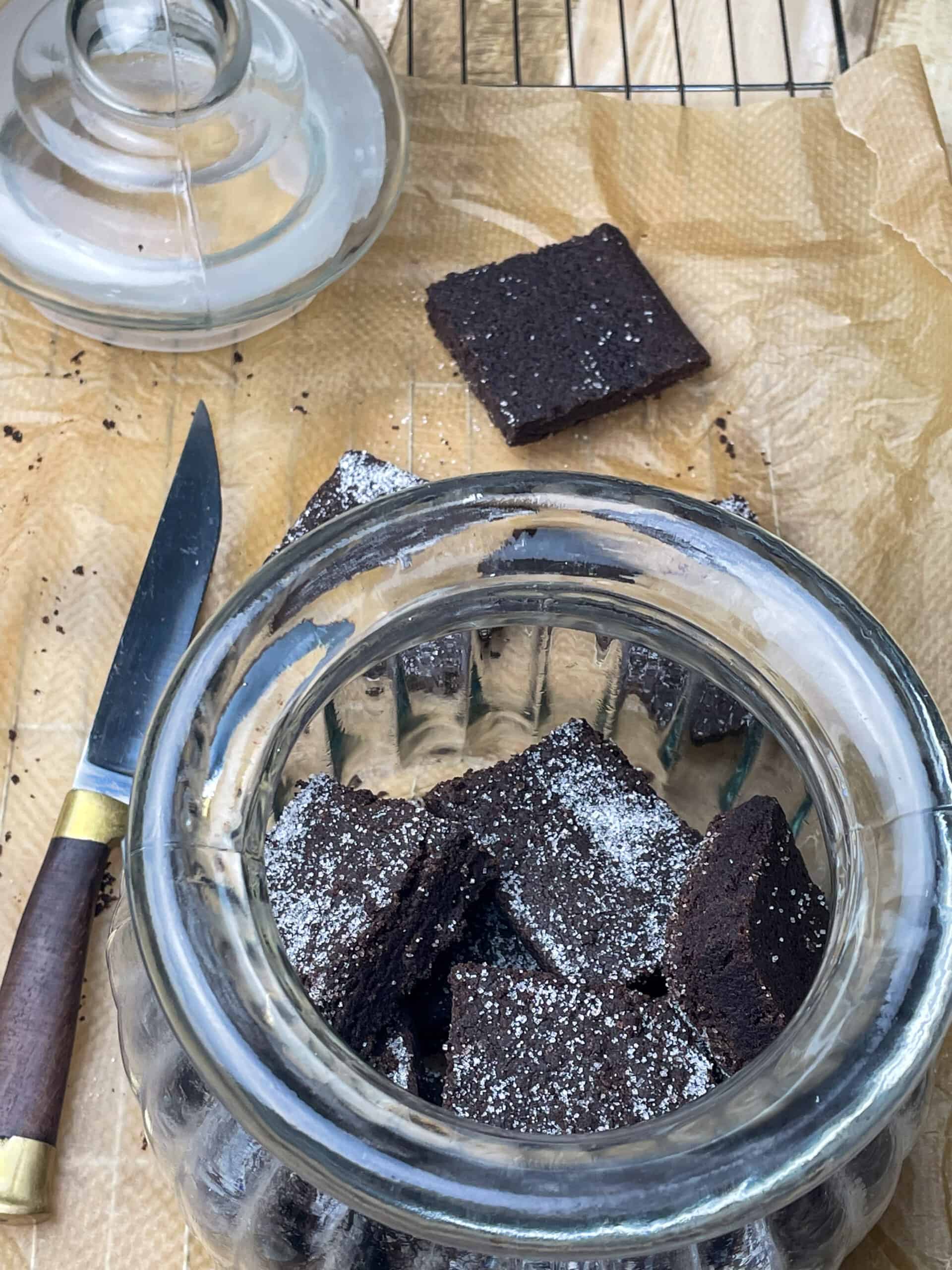 Concrete cake in a glass jar, with knife to side and lid on top of baking paper, single biscuit out of the jar.