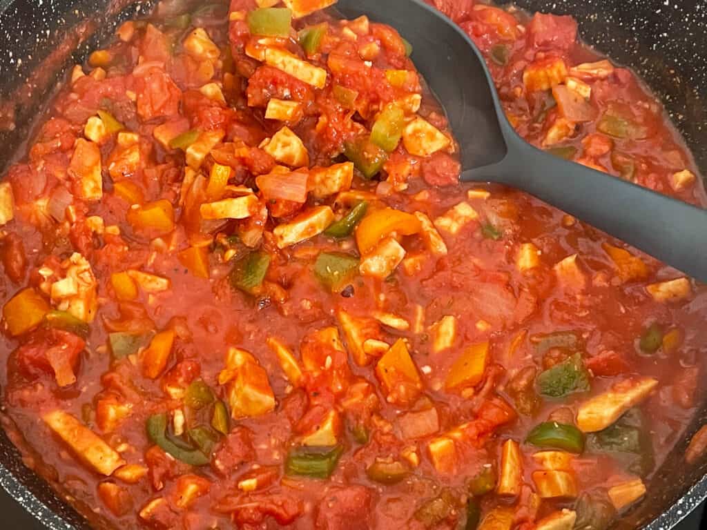 Bolognese sauce cooking in skillet with black ladle.