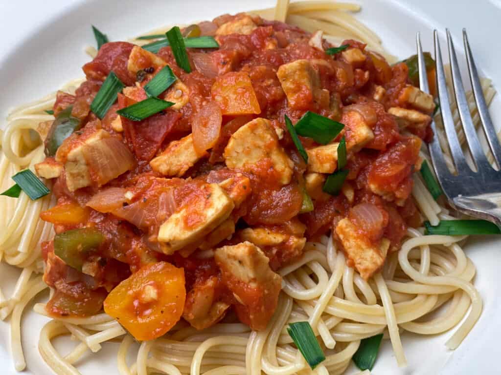 Tempeh Bolognese served on spaghetti pasta in white bowl and silver fork to side.