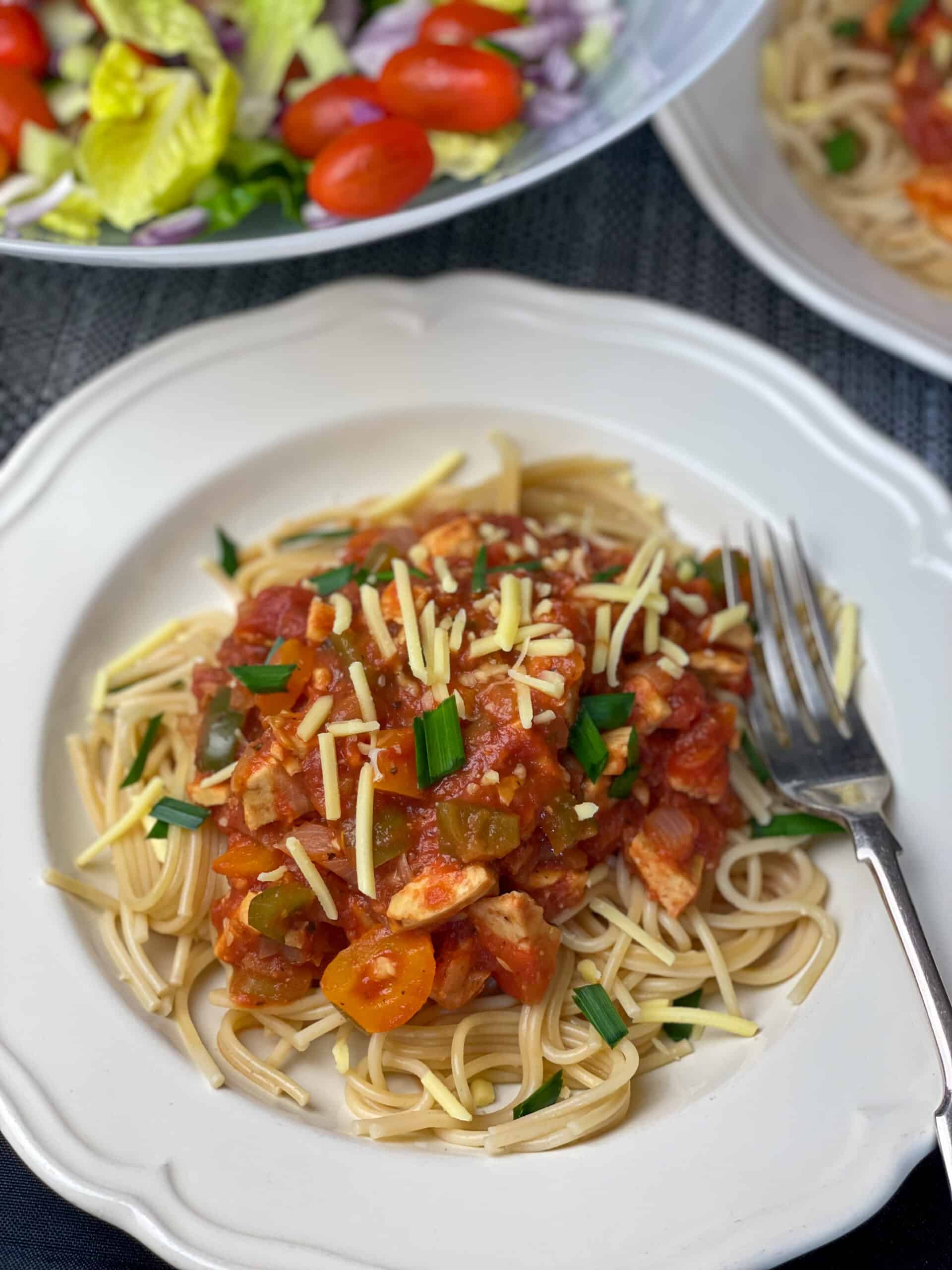 bowl of tempeh Bolognese with silver fork and salad to side.