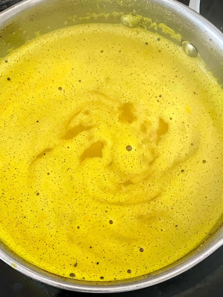 turmeric latte ingredients mixed and simmering in saucepan.