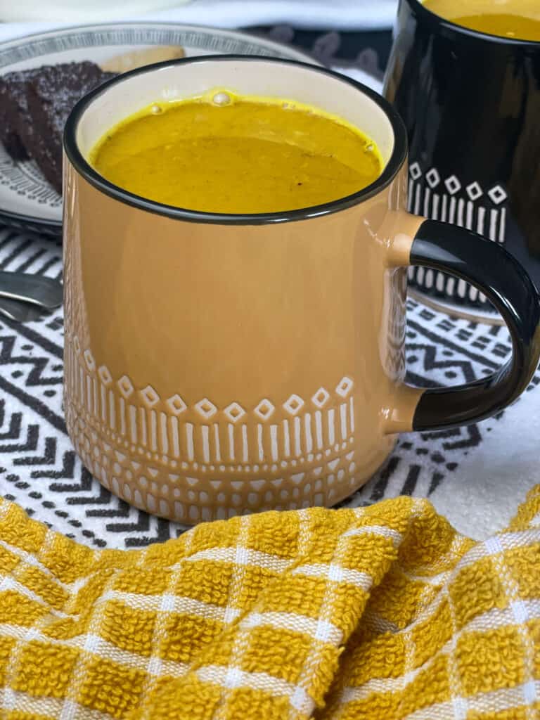 turmeric latte served in large yellow mug with white pattern, yellow check tea towel and black and white tea towel.