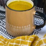 turmeric latte served in large yellow mug with white pattern, yellow check tea towel and black and white tea towel.